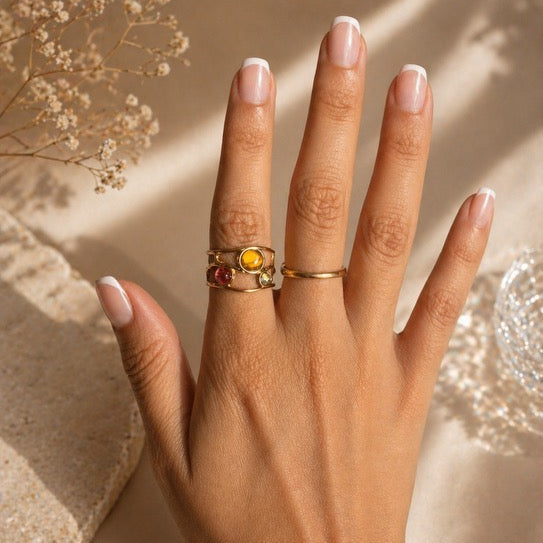 Hand wearing an eye catching gold rings with multicoloured gemstones on a neutral background