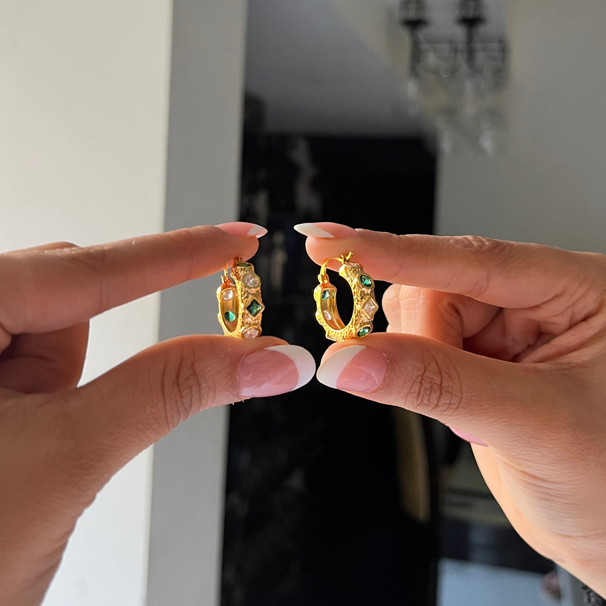 Green and white stone gold hoops held by a hand