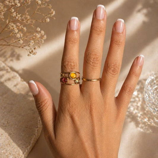Hand wearing an eye catching gold rings with multicoloured gemstones on a neutral background