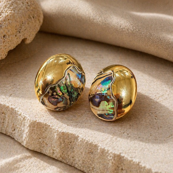Statement gold earrings with iridescent finish on a beige fabric background