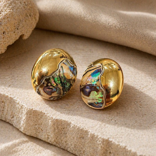 Statement gold earrings with iridescent finish on a beige fabric background
