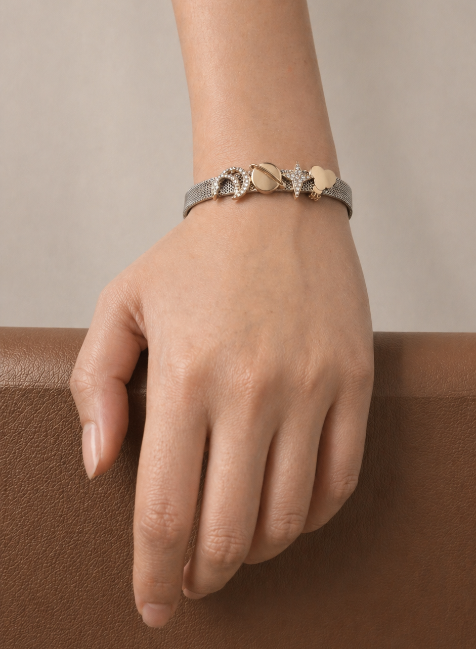 Hand wearing a silver bracelet with gold coloured star and moon designs on a neutral background
