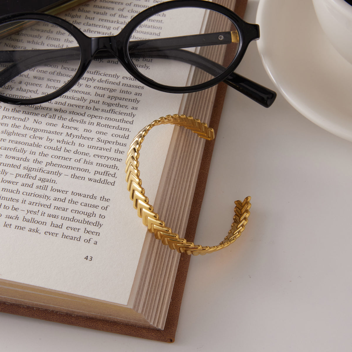 a golden bracelet placed with a book and a pair of glasses