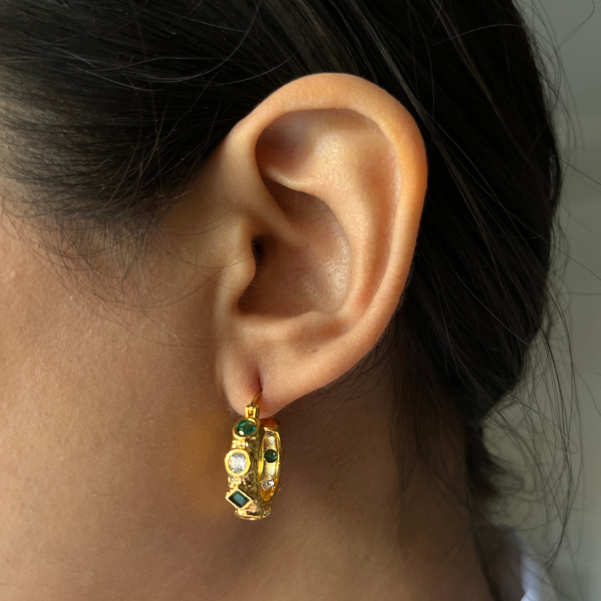 Close-up of an ear wearing a gold earring with green gemstones.