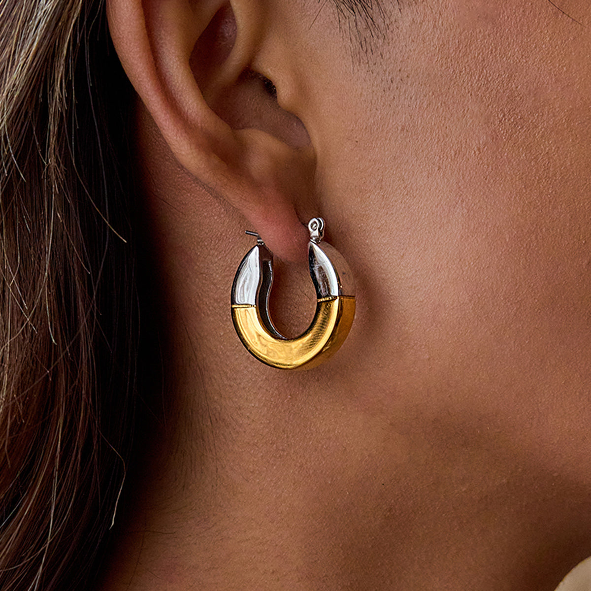 Close-up of a person wearing gold and silver hoop earrings.