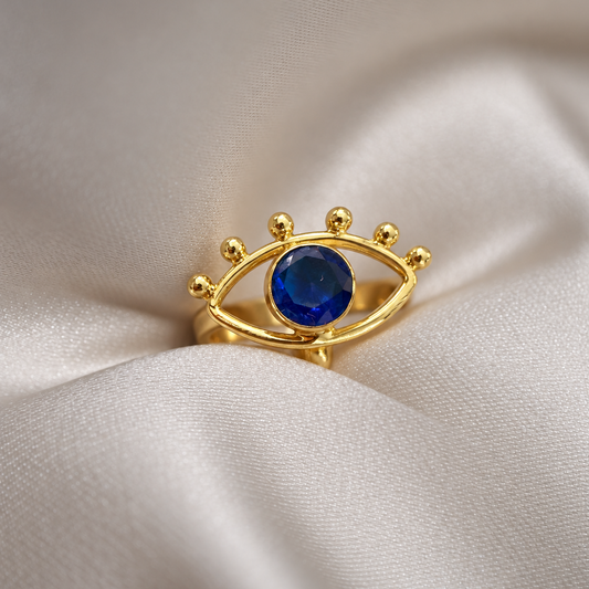 Nazar Ring resting on a cream surface with its blue centre stone facing forward