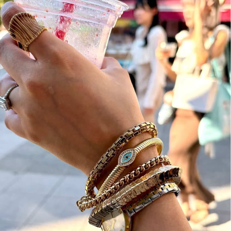 A close-up of a person's wrist wearing our Jaali ring and a stack of gold-toned bracelets and a watch.