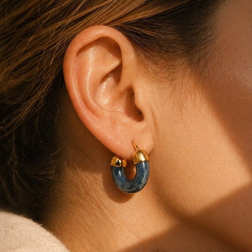 Close-up of an ear wearing a blue hoop earring with gold accents.