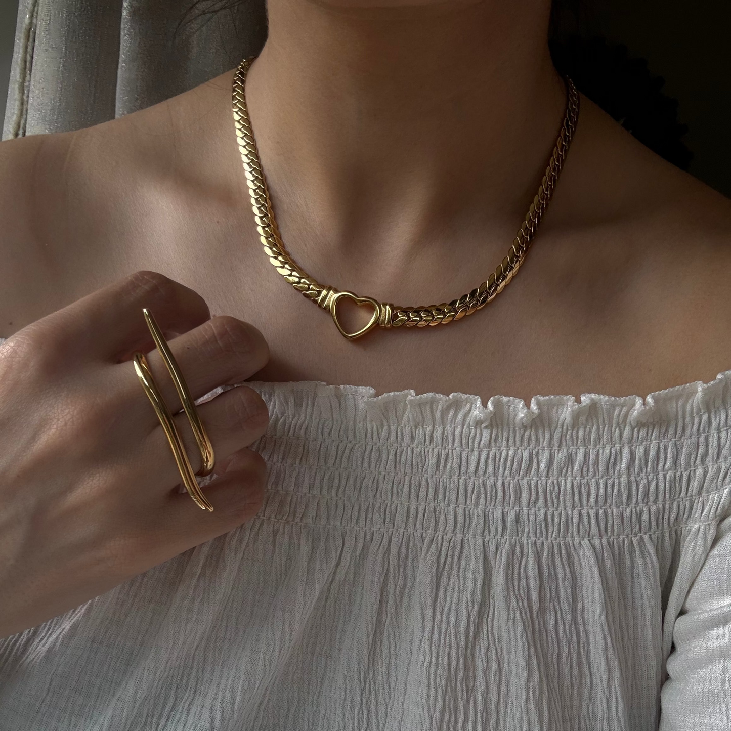 Person wearing a gold chain necklace and ring, with a white off-shoulder top.