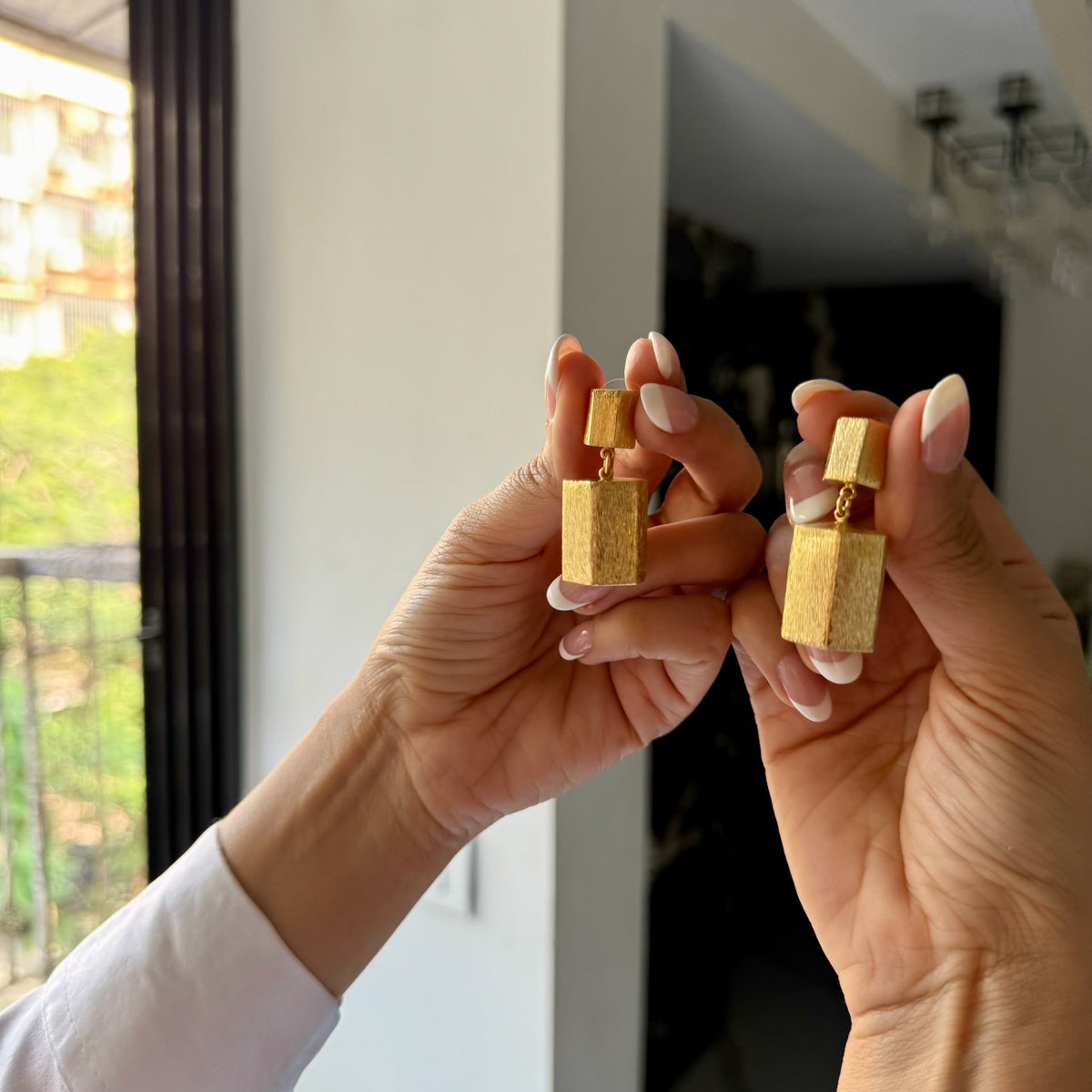Gold earrings held up to a mirror with a blurred indoor background