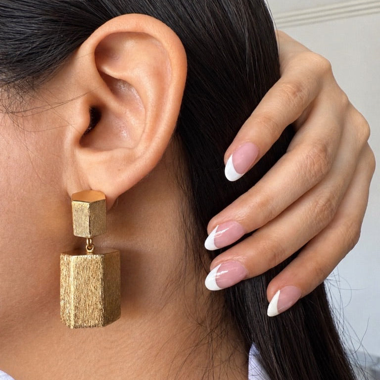 Close-up of a person wearing gold geometrical earrings with a neutral background
