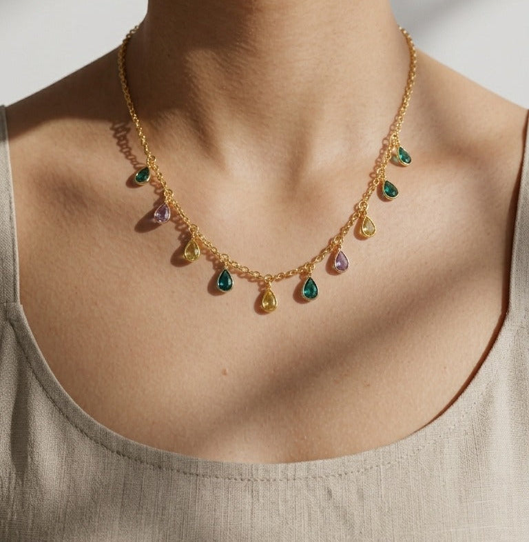 Close-up of a person wearing a gold necklace with green gemstones on a neutral background