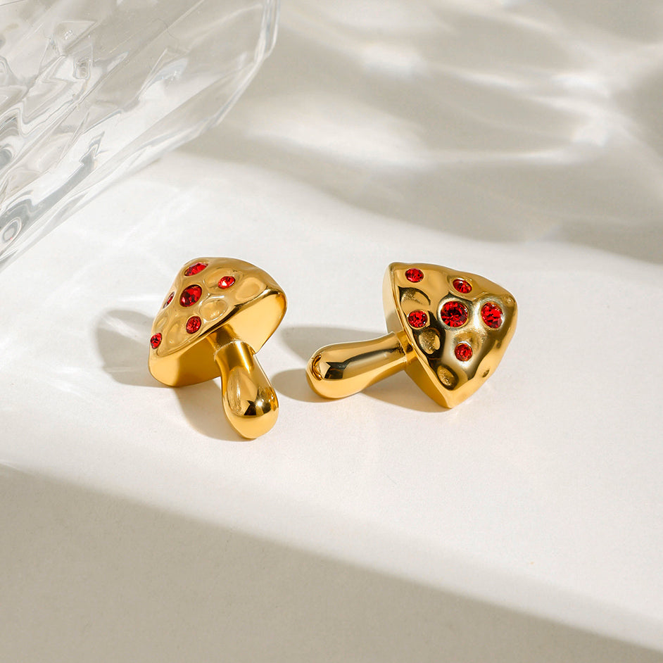 Gold mushroom-shaped earrings with red gemstones on a white surface
