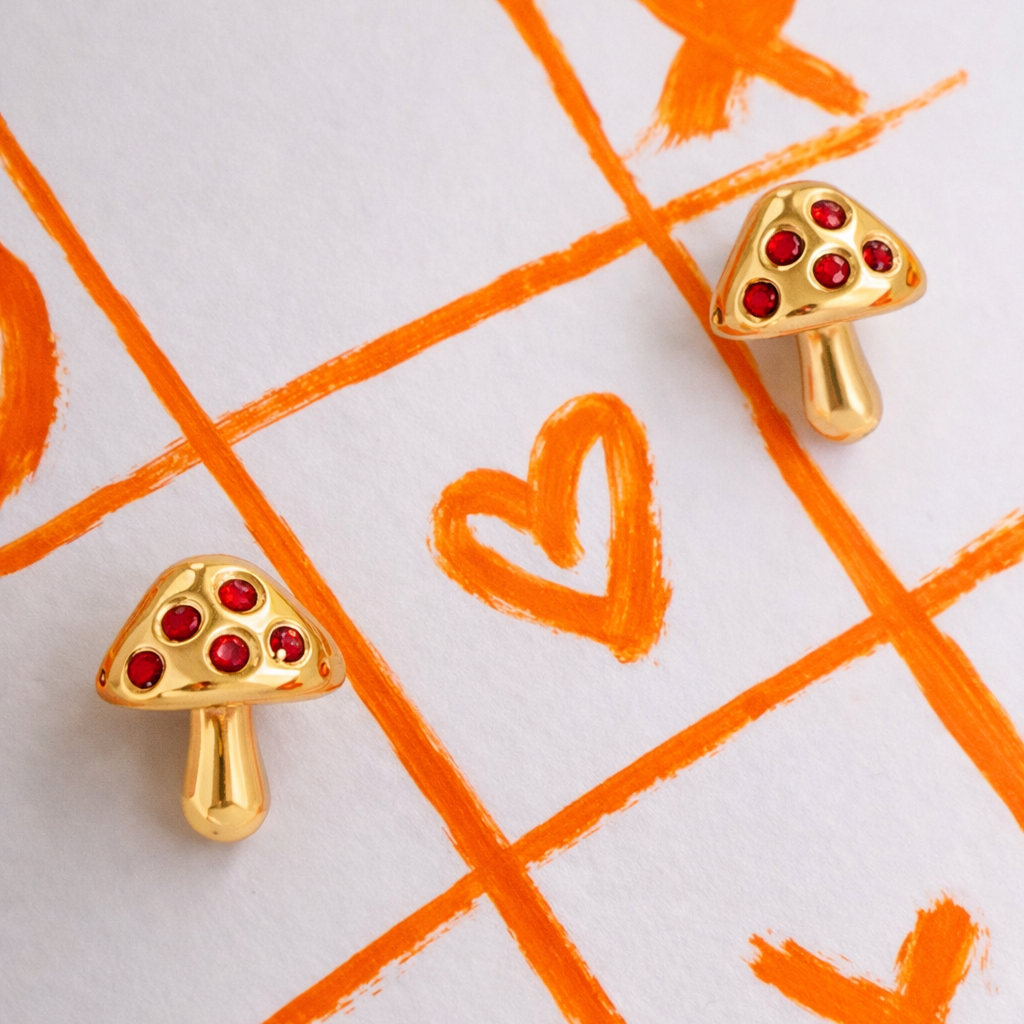 Gold mushroom-shaped earrings with red gemstones on a white background 