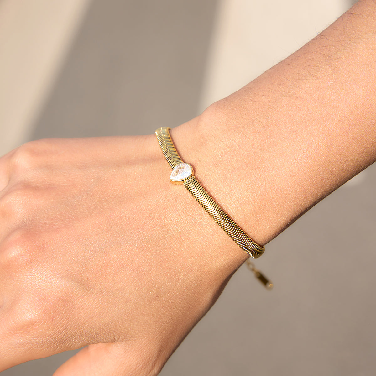 Pear shaped stone in the centre, snake chain on a person's wrist