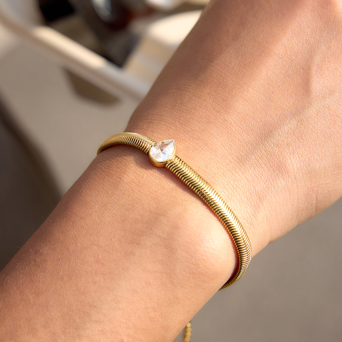 Pear shaped stone in the centre, snake chain on a person's wrist