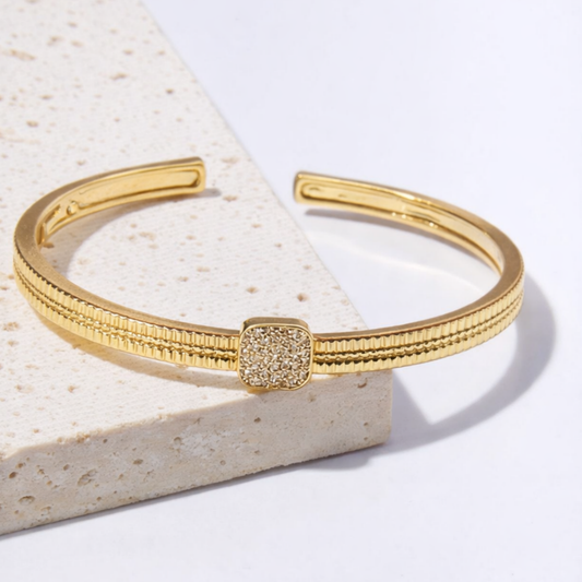 Gold bracelet with a textured design on a light stone surface
