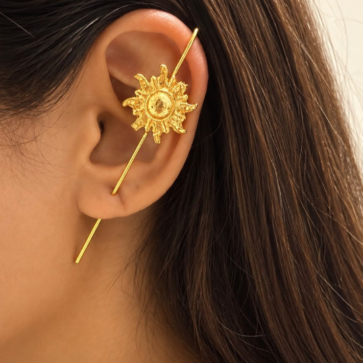 A close-up of a model's ear wearing a gold ear cuff with a sunburst design and a matching gold chain necklace with sunburst charms.