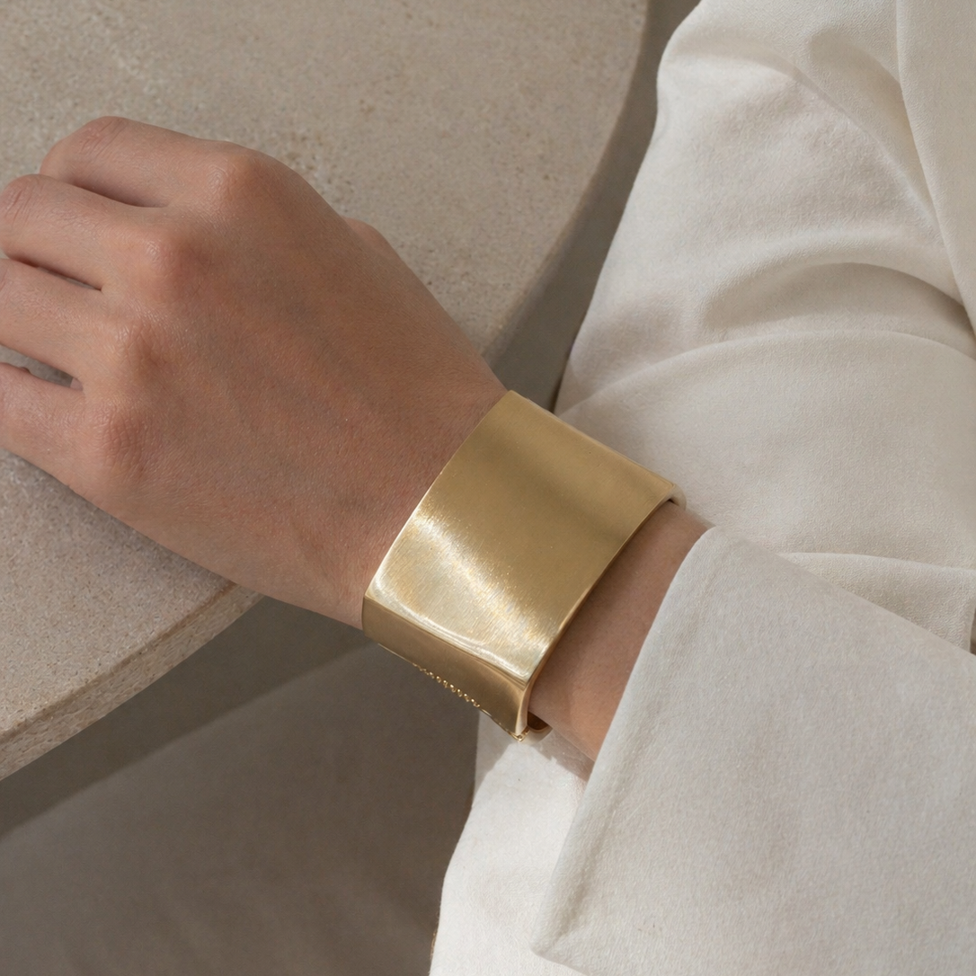 Statement chunky gold bracelet on a person's wrist with a neutral background