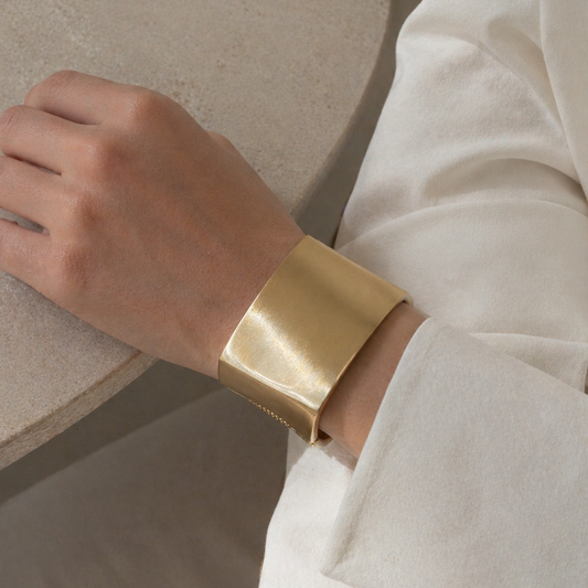 Statement chunky gold bracelet on a person's wrist with a neutral background