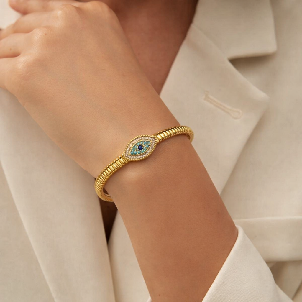 Gold bracelet with a blue gemstone on a person's wrist, wearing a white outfit.